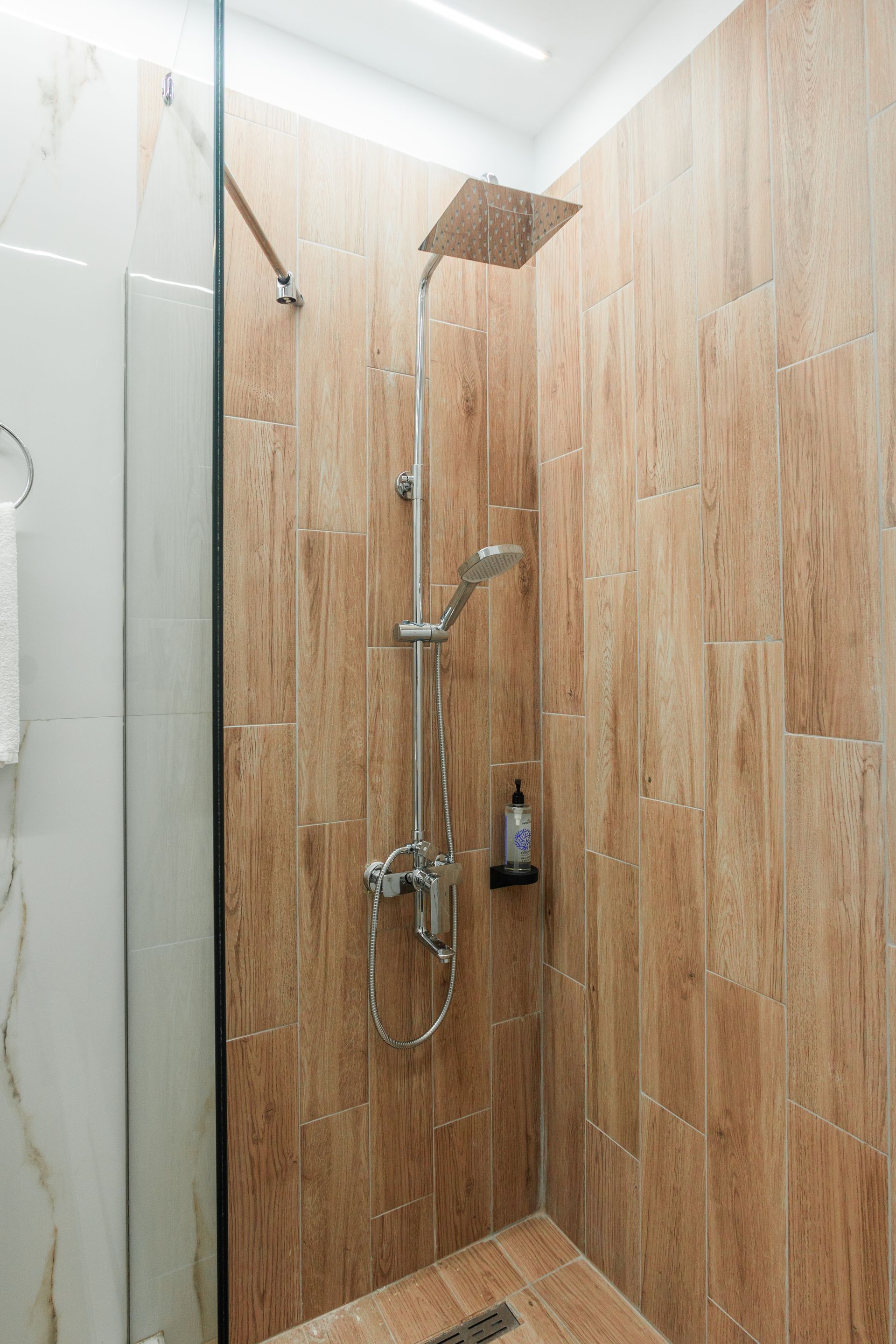 Shower with wood-look tile walls, chrome fixtures, and glass enclosure.