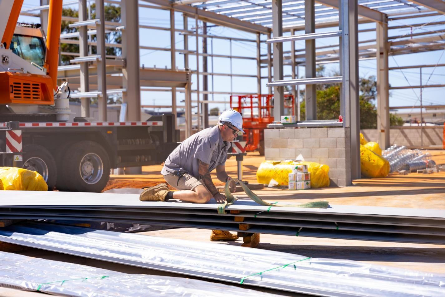 A Man is Working on a Stack of Metal Sheets at a Construction Site — Roofing Contractor in Port Macquarie, NSW