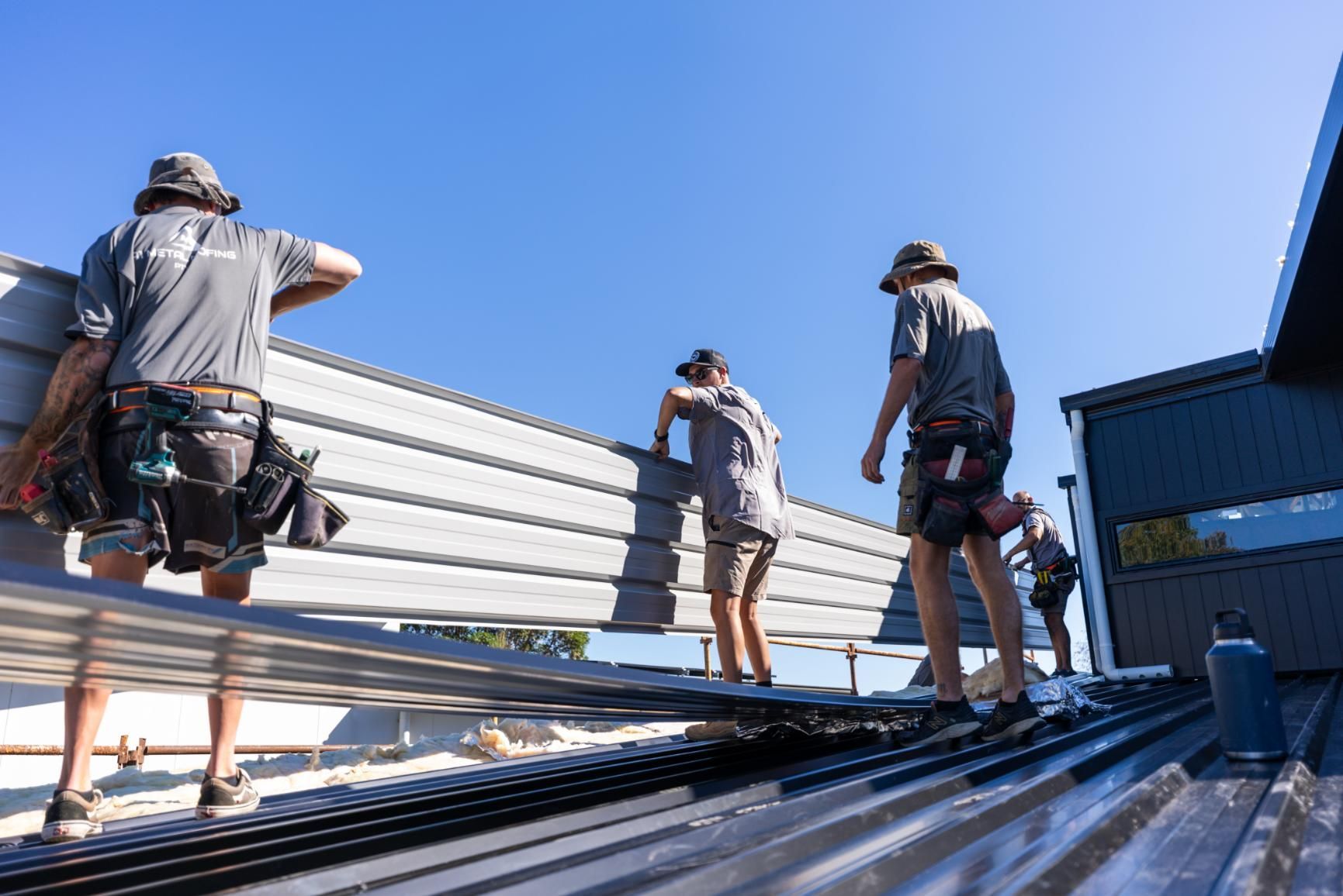 A Group of Construction Workers are Working on the Roof of a Building — Roofing Contractor in Laurieton, NSW