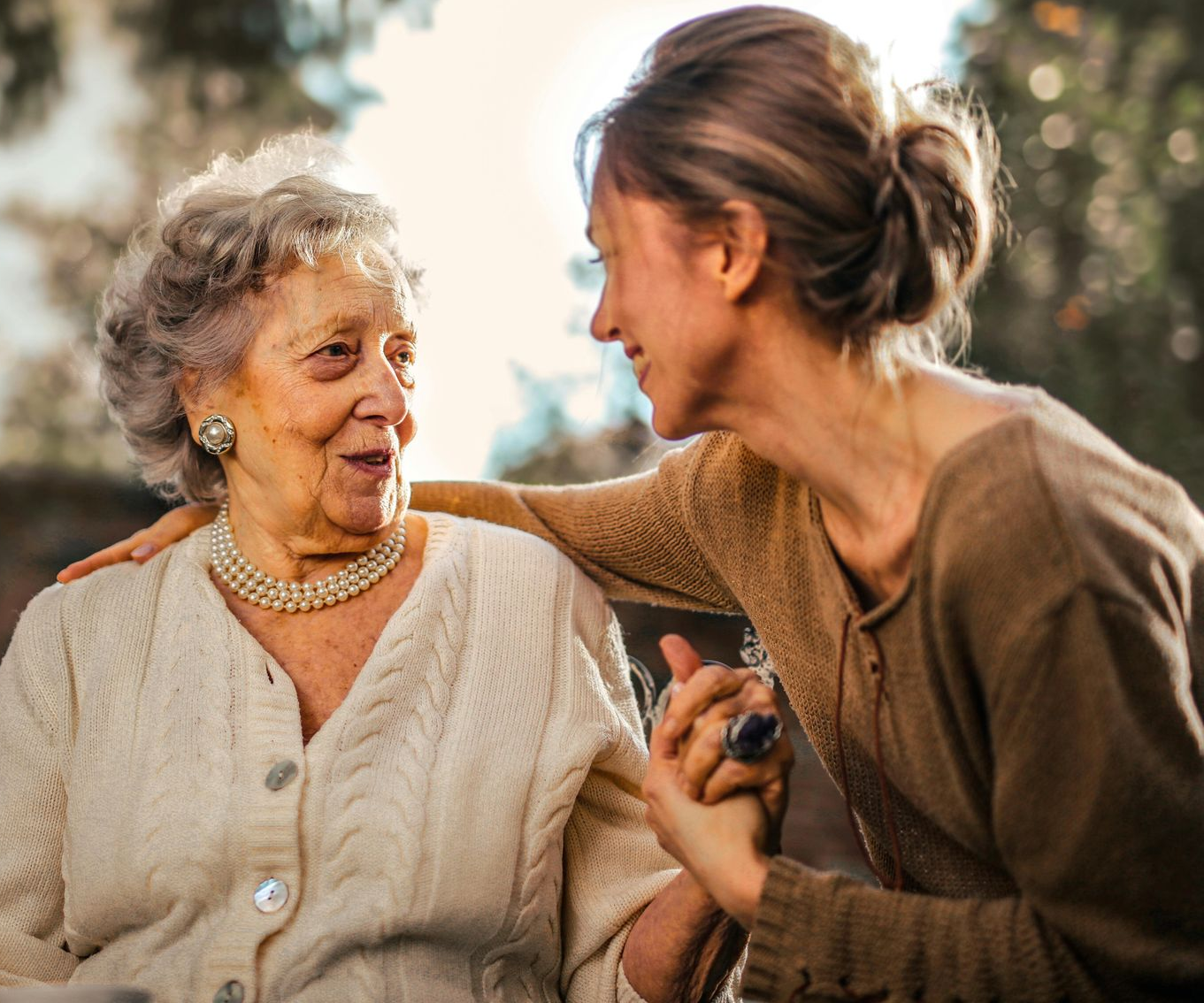 Two people in warm-toned clothing holding hands and sharing a gentle, connected gaze in a soft-focus, outdoor setting.