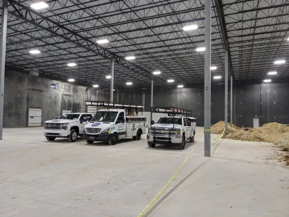 Construction warehouse interior with three white pickup trucks parked on a concrete floor.