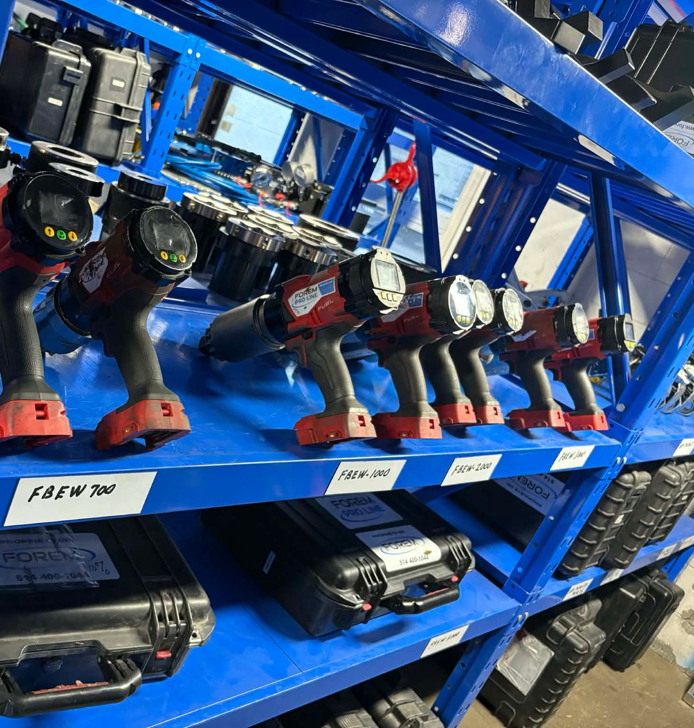 Des outils électriques rouges alignés sur des étagères industrielles en métal bleu, avec des coffrets de rangement sur les étagères inférieures.