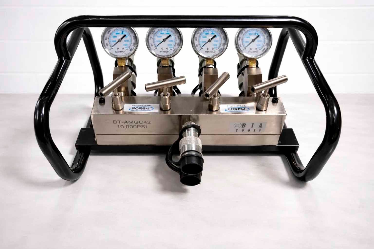 Un collecteur métallique avec quatre manomètres, des vannes et un raccord pour tuyau de pression, monté dans une cage de protection noire.