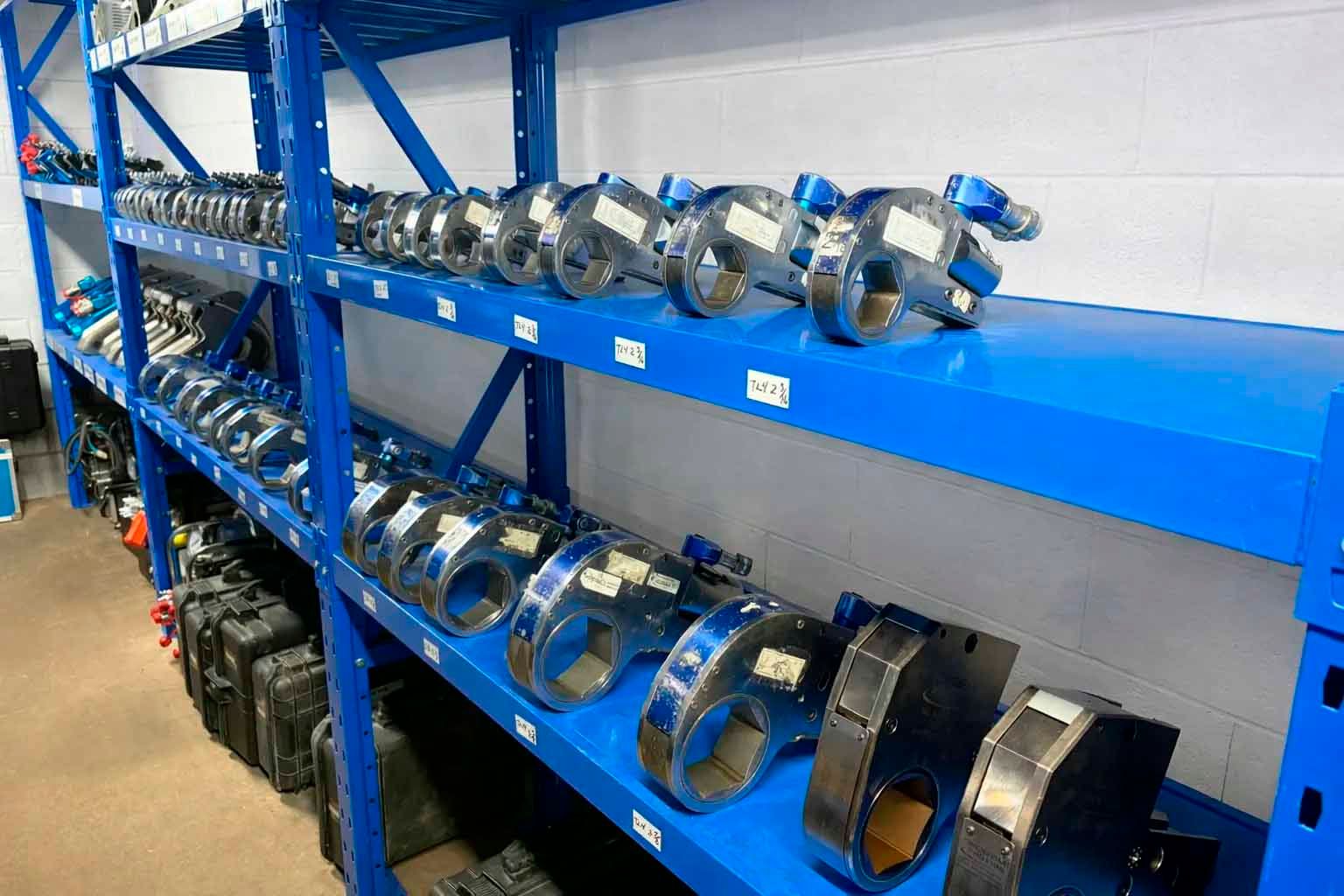 Étagère métallique bleue contenant des rangées de pièces industrielles argentées et noires.