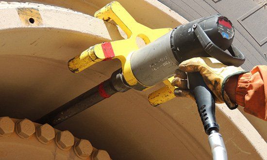 Une personne utilise une clé à chocs jaune et grise pour retirer des boulons d'une grosse machine.