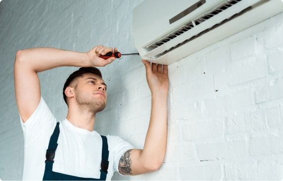 A man is fixing an air conditioner on the wall with a screwdriver.