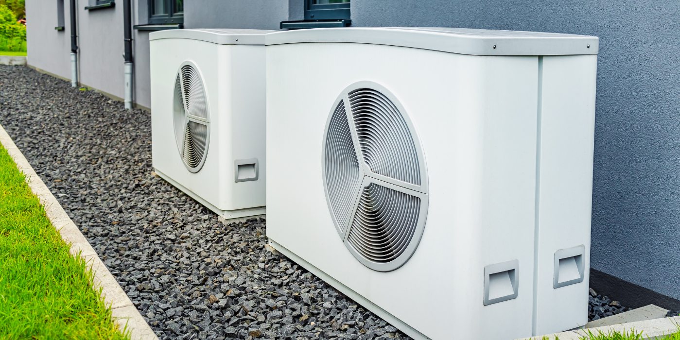 Two air conditioners are sitting next to each other on the side of a building.