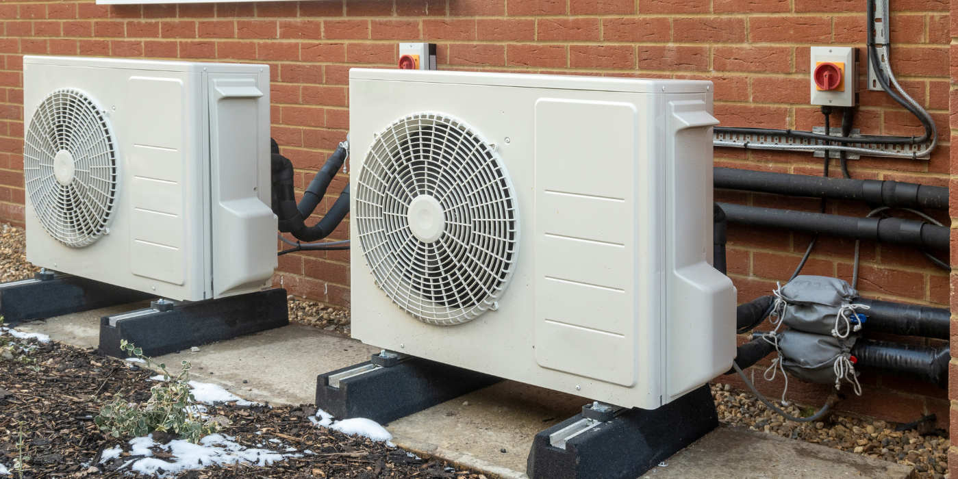 Two air conditioners are sitting outside of a brick building.