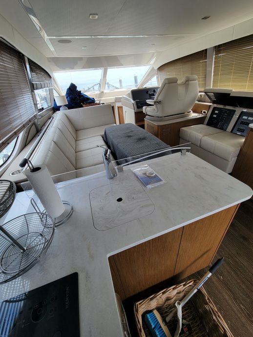 A modern boat interior featuring a cream-colored couch, a countertop with a paper towel holder, and pilot chairs ahead.