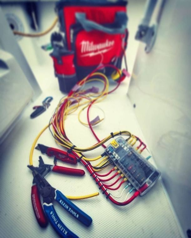 Electrical wiring project featuring a Milwaukee tool bag, fuse block, and hand tools arranged on a white boat deck.