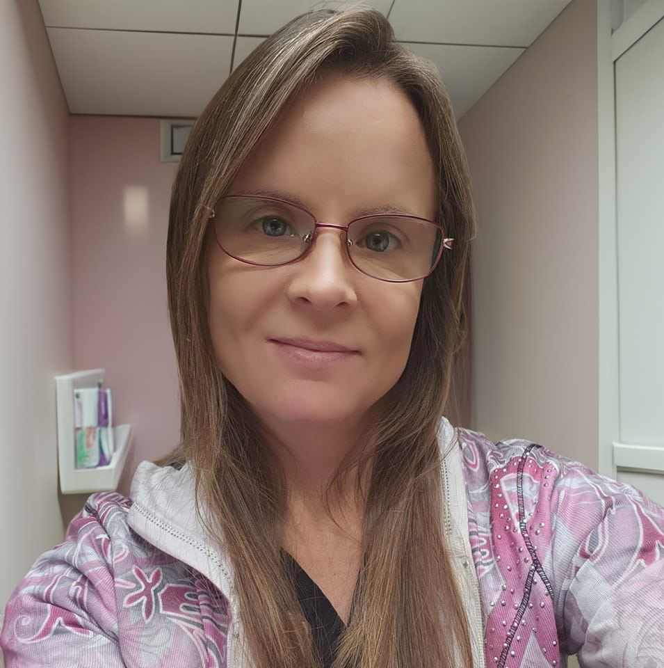 A woman wearing glasses and a pink jacket is taking a selfie.