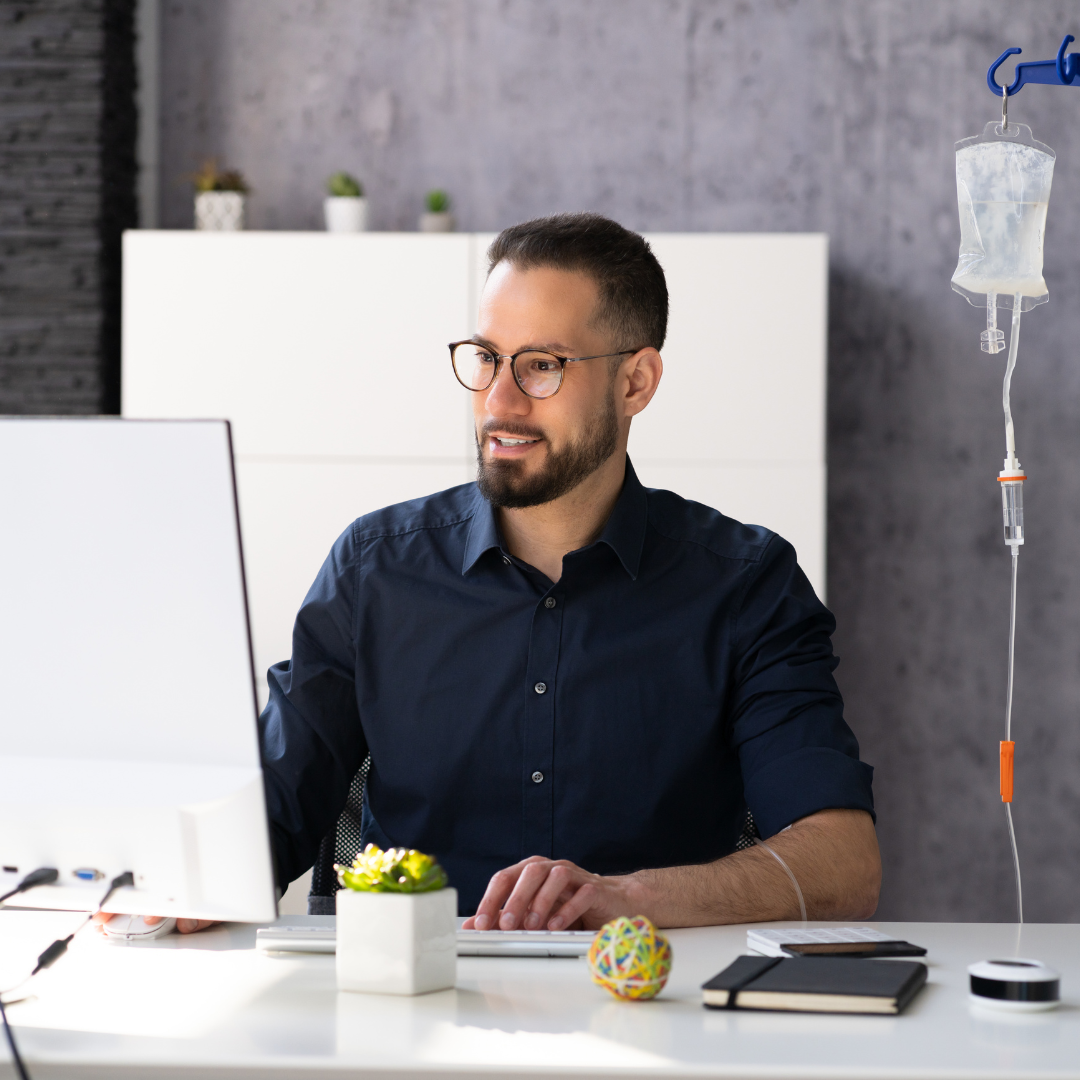 A man wearing glasses is sitting at a desk in front of a computer