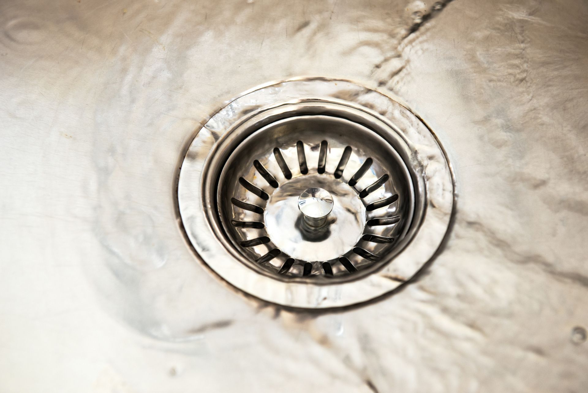 A close-up of a metal sink drain with water flowing around it. A close-up of a metal sink drain with water flowing around it.