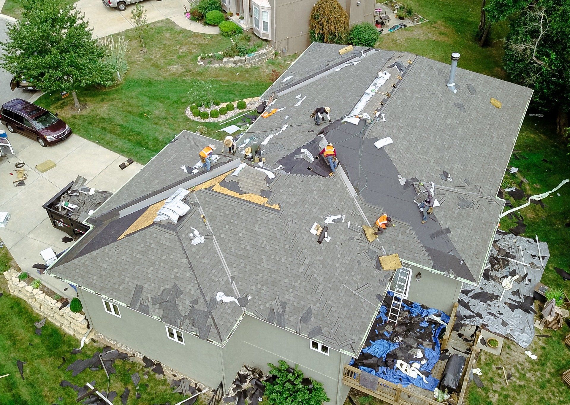 Roofers working on a gray-shingled house, removing damaged areas and applying new roofing.