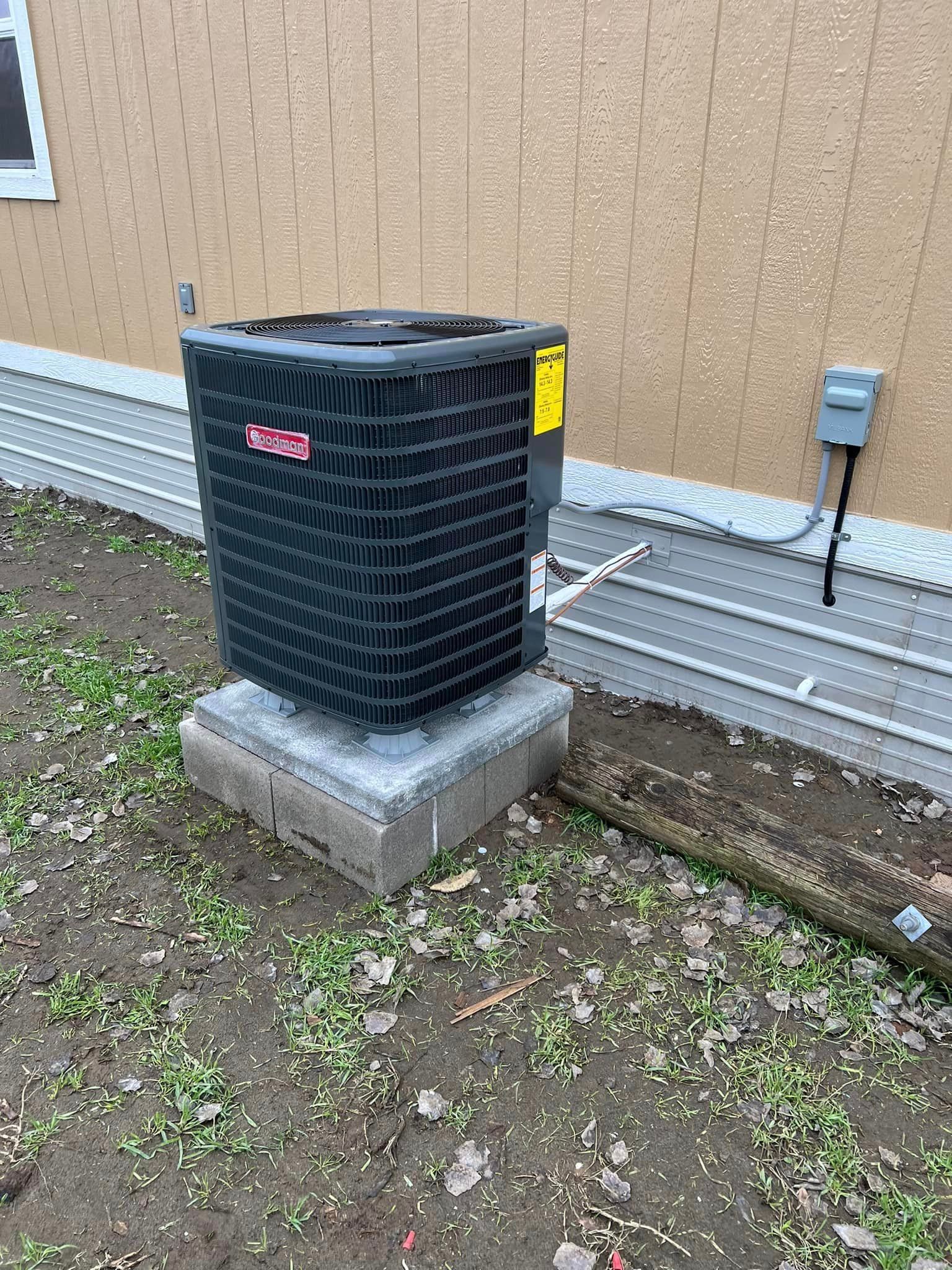A black air conditioner is sitting on a concrete block in front of a house.
