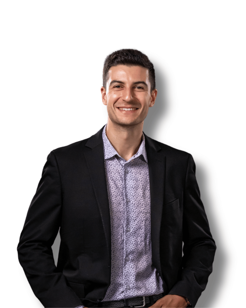 A person wearing a patterned dress shirt and a black blazer against a plain background.