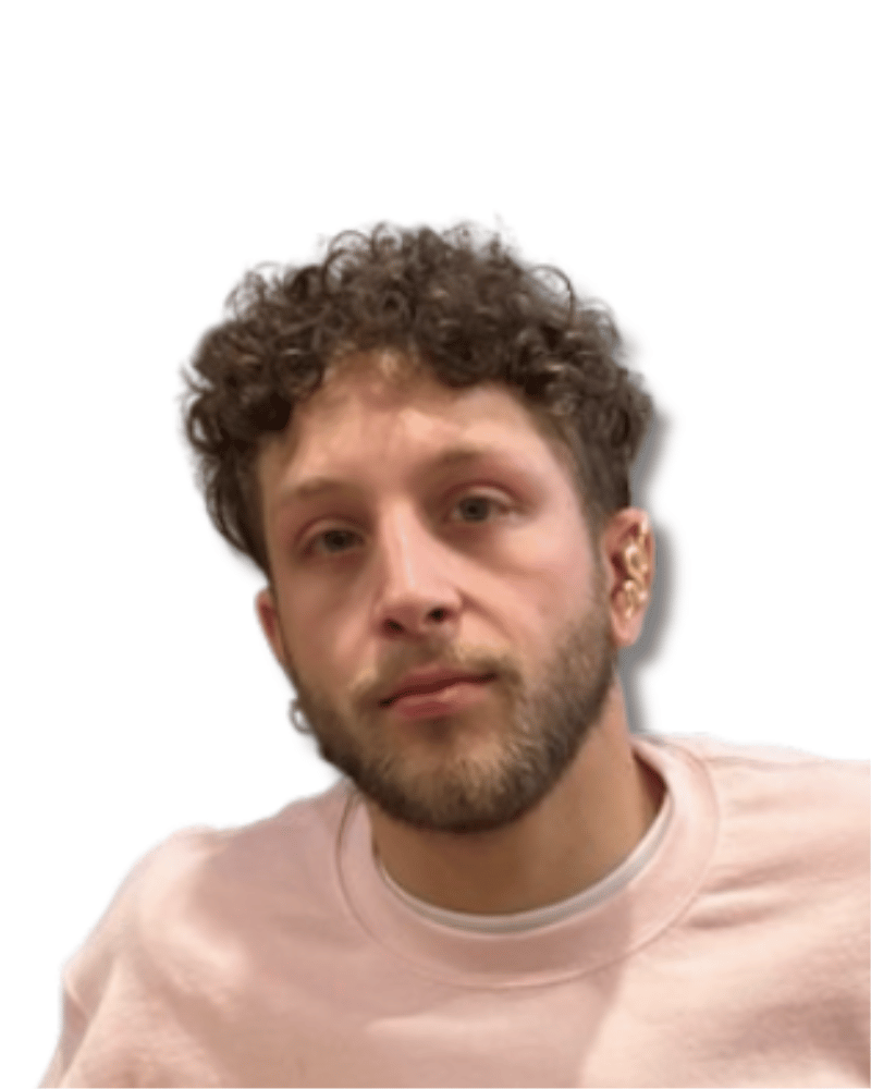 A person with curly hair and a beard, wearing a light pink shirt.