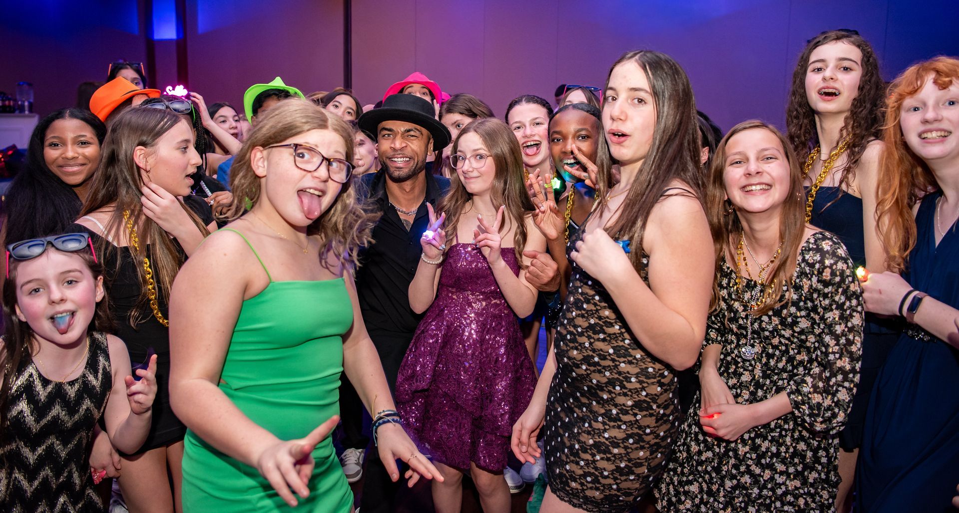 A man in a graphic shirt and khakis smiles excitedly at a party surrounded by people in semi-formal attire.