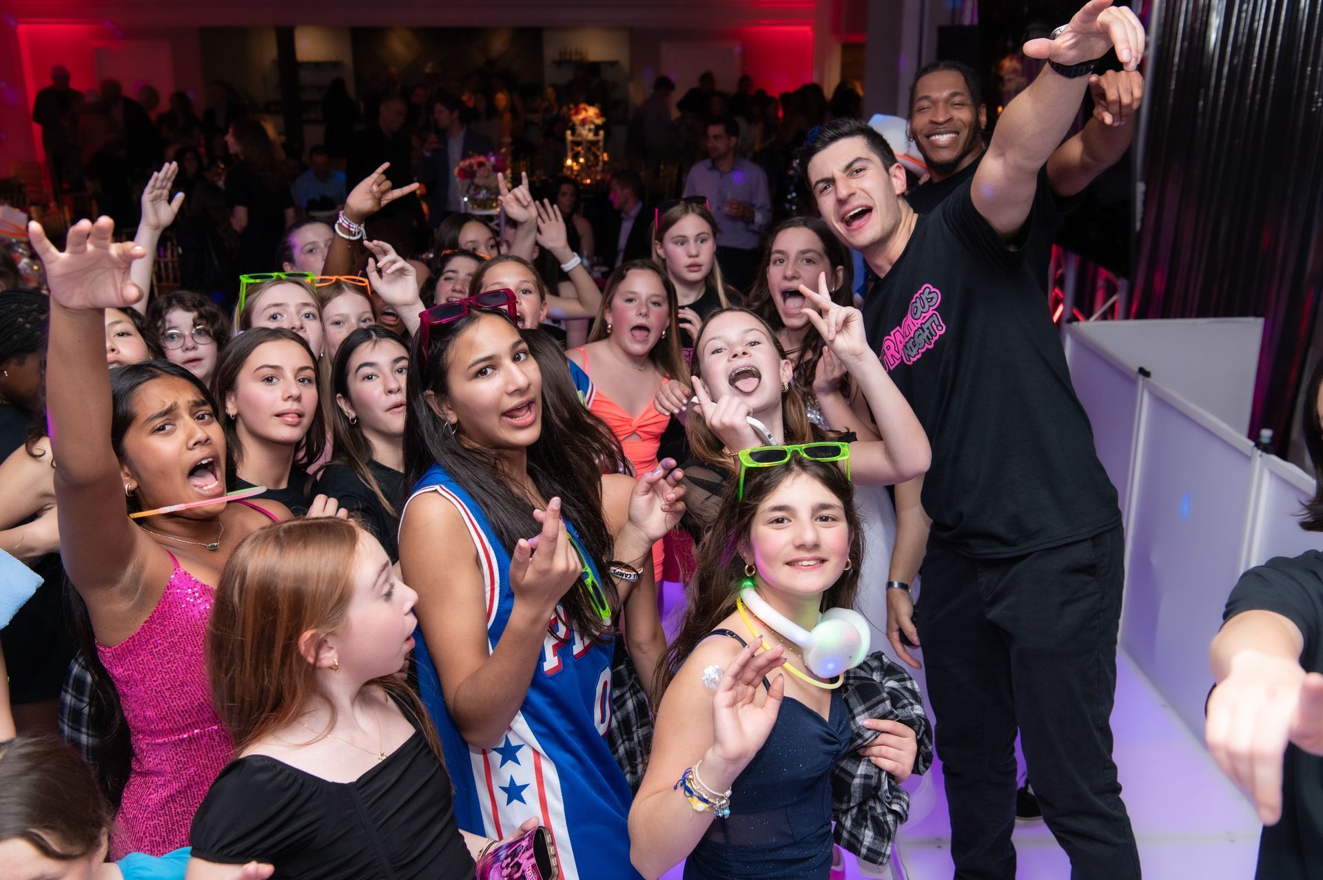 Guests celebrating and dancing at a lively Mitzvah party with a DJ, vibrant lighting, and entertainment creating a fun atmosphere.