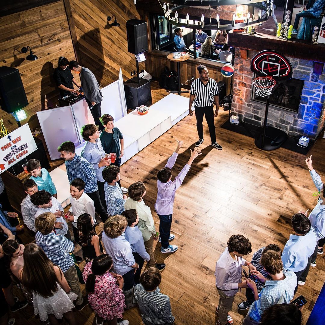 Guests participating in a basketball shooting game at a Mitzvah celebration with DJ and referee.