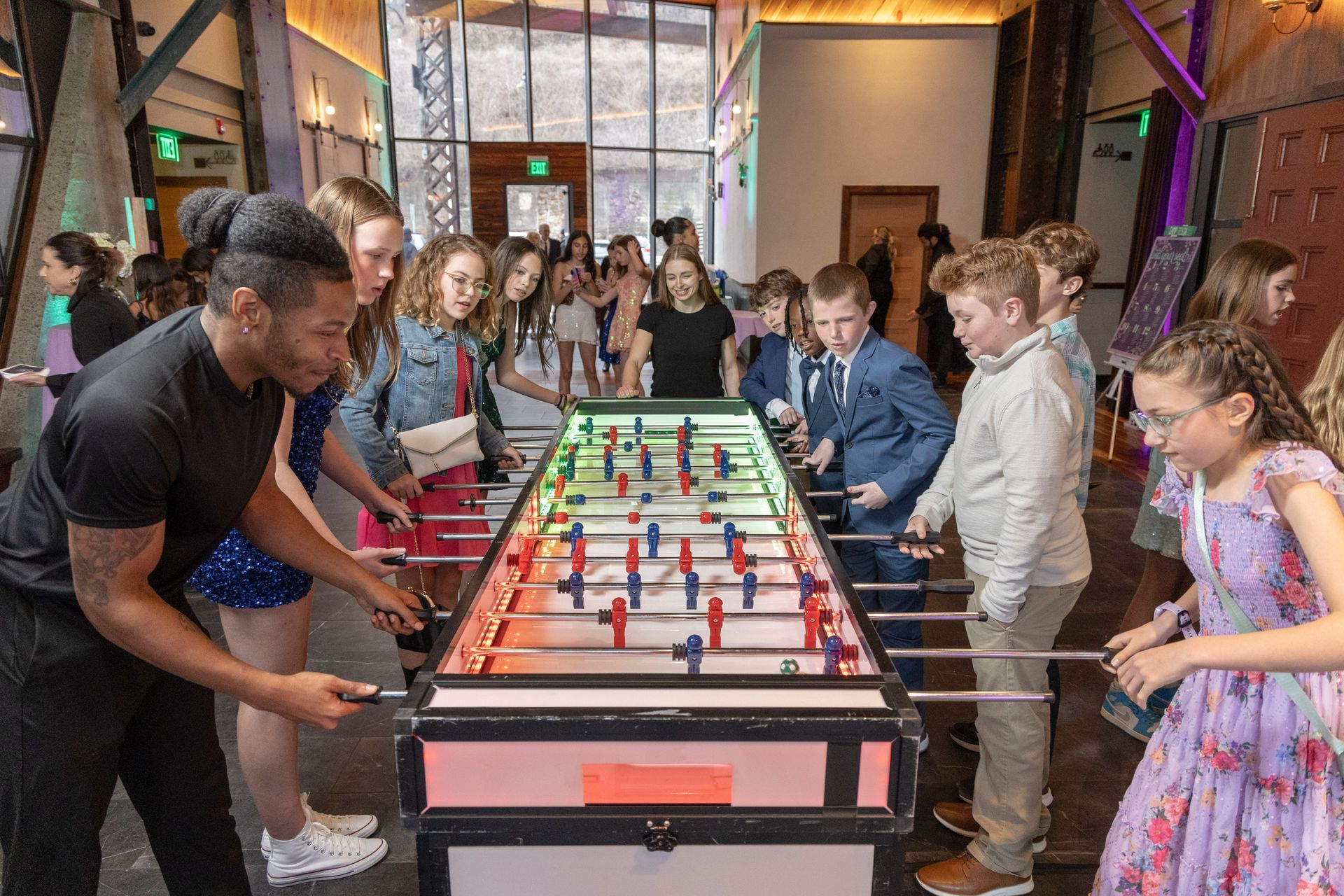 Guests engaging in a colorful, illuminated foosball game at a lively event, capturing playful competition and entertainment for young attendees.
