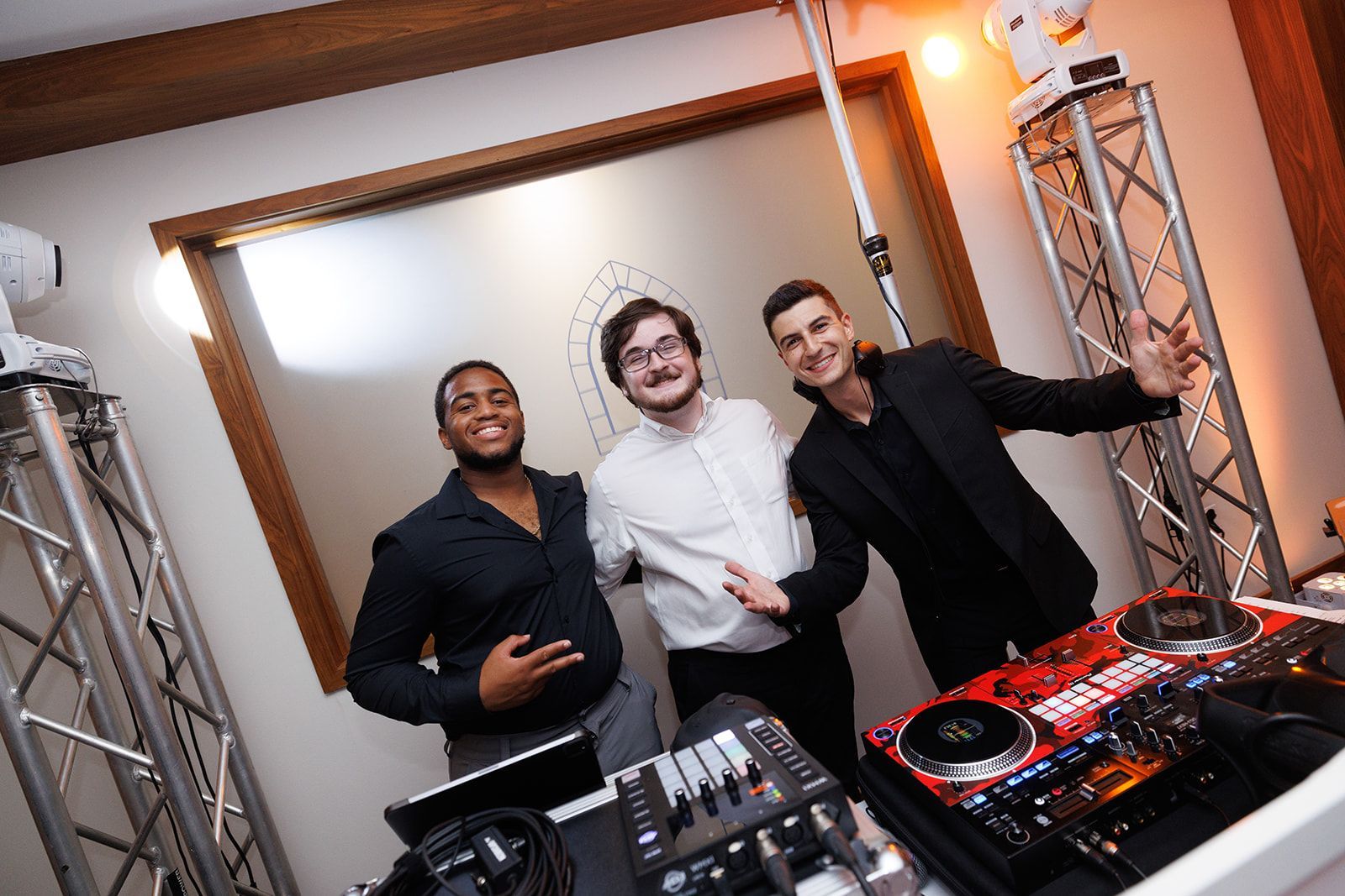 Three DJs pose together behind their booth during a wedding reception setup.