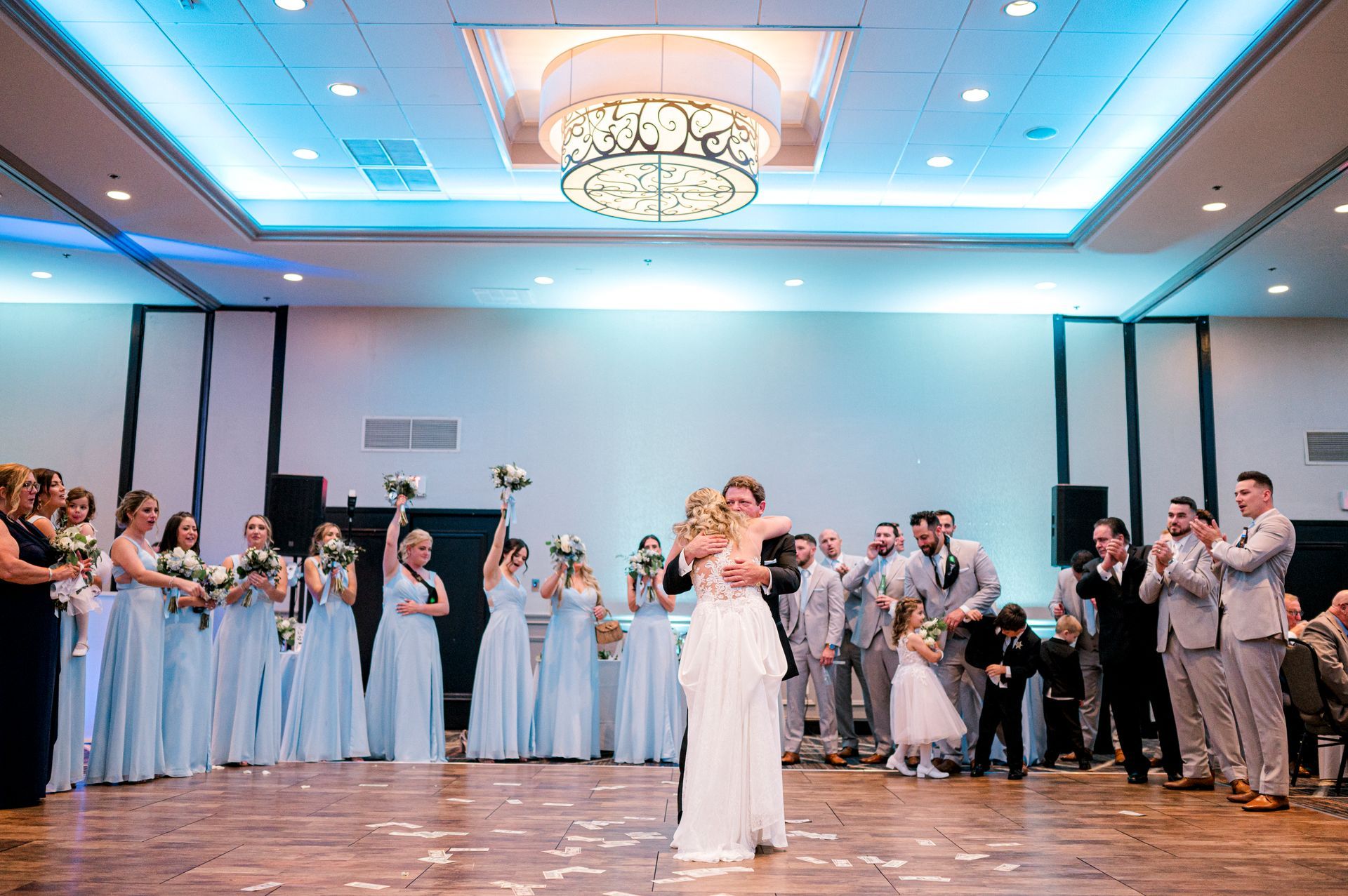 A bride and groom are dancing in front of their wedding party in a large room.