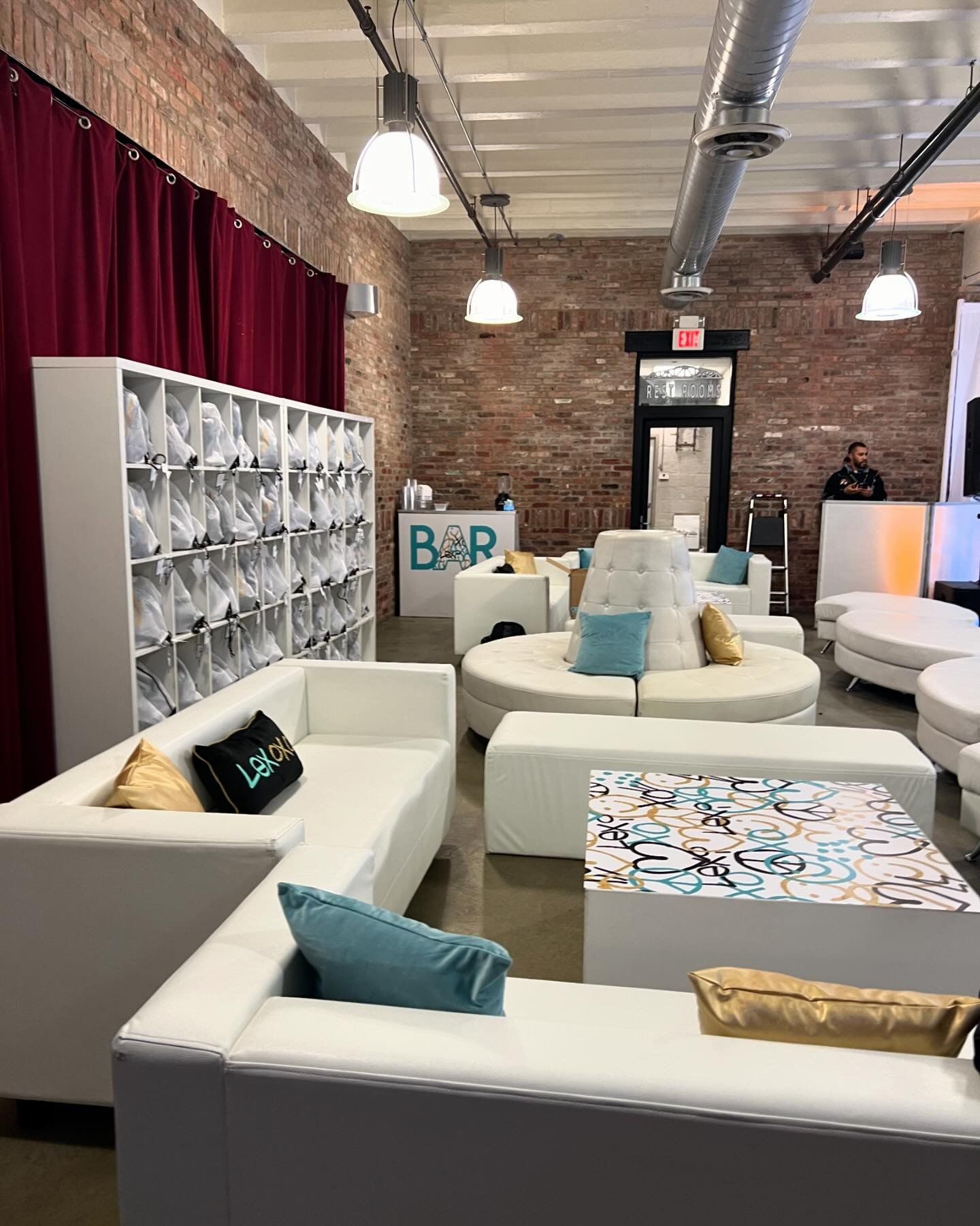 Indoor lounge setup with white leather couches, custom pillows, and a cubby wall.