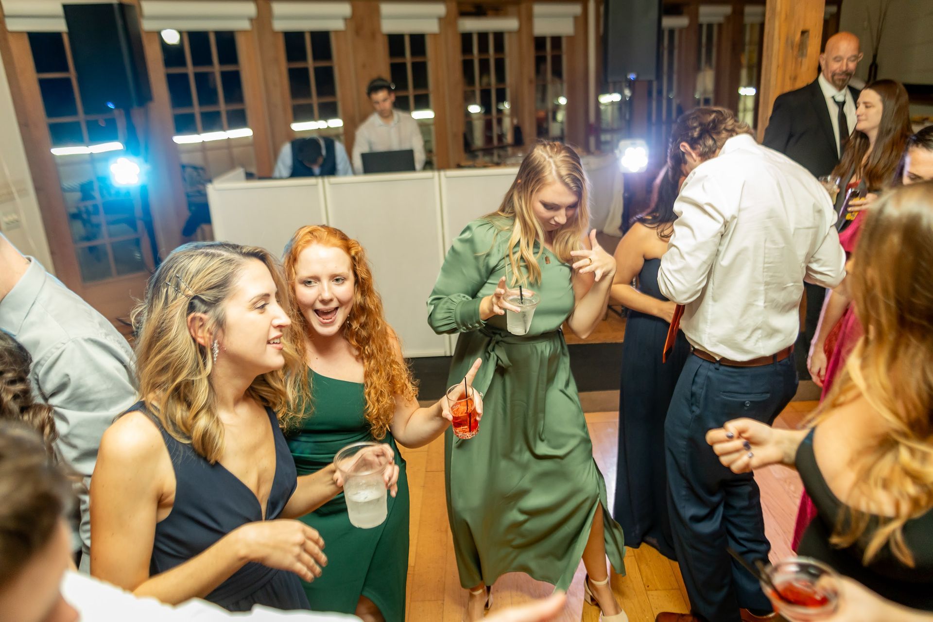 Guests dancing with drinks in hand while the DJ performs in the background during the wedding party.