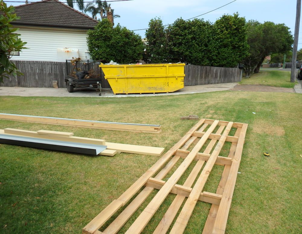 A yellow dumpster is sitting in the grass next to some wooden pallets — Bins on Rims in Kempsey, NSW