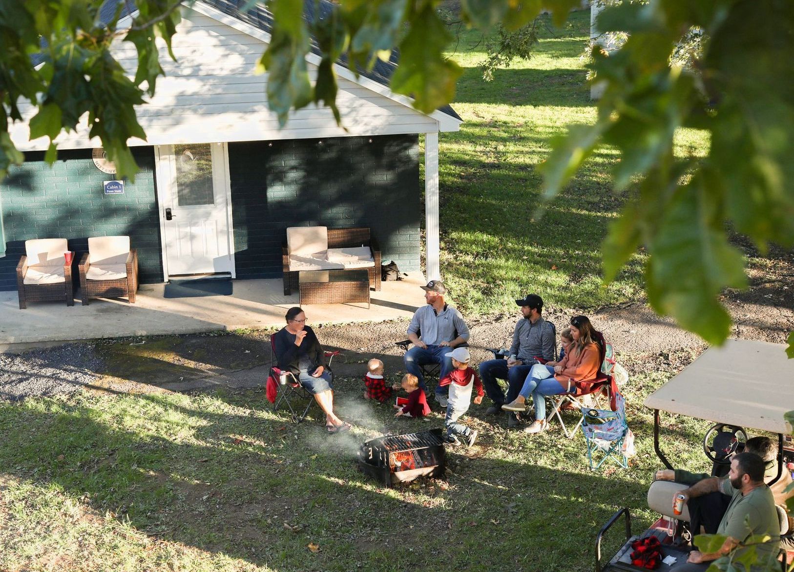 A group of people are sitting around a fire pit in front of a house.