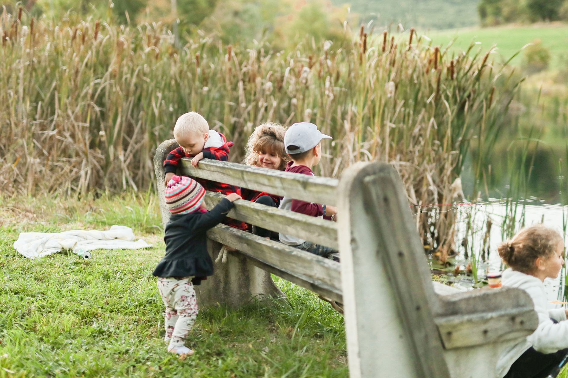 A group of children are sitting on a wooden bench near a lake.