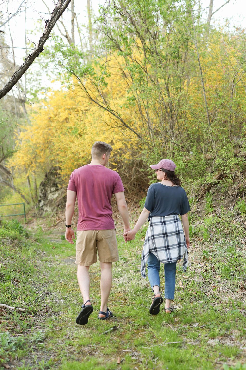 A man and a woman are walking down a forest path holding hands.