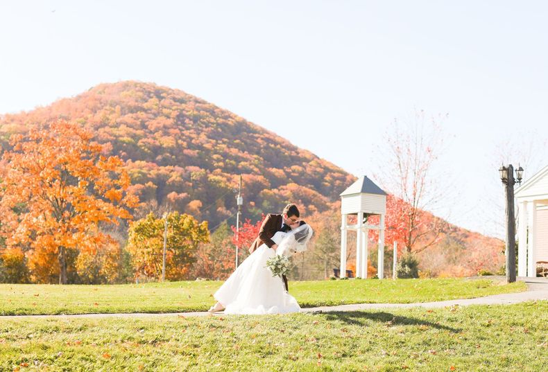 A bride and groom are dancing in a field with a mountain in the background.