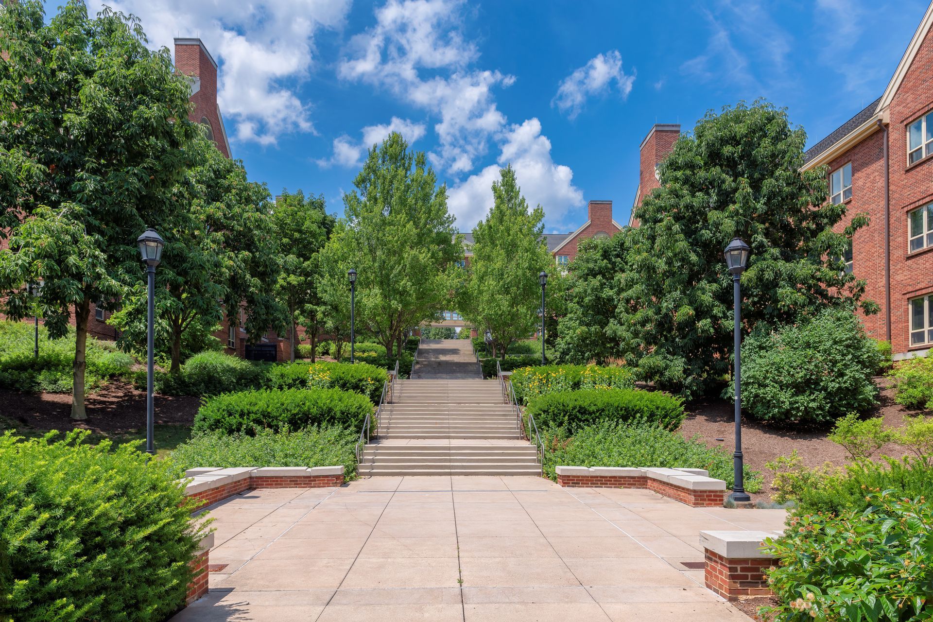 A brick building with stairs leading up to it is surrounded by trees and bushes.