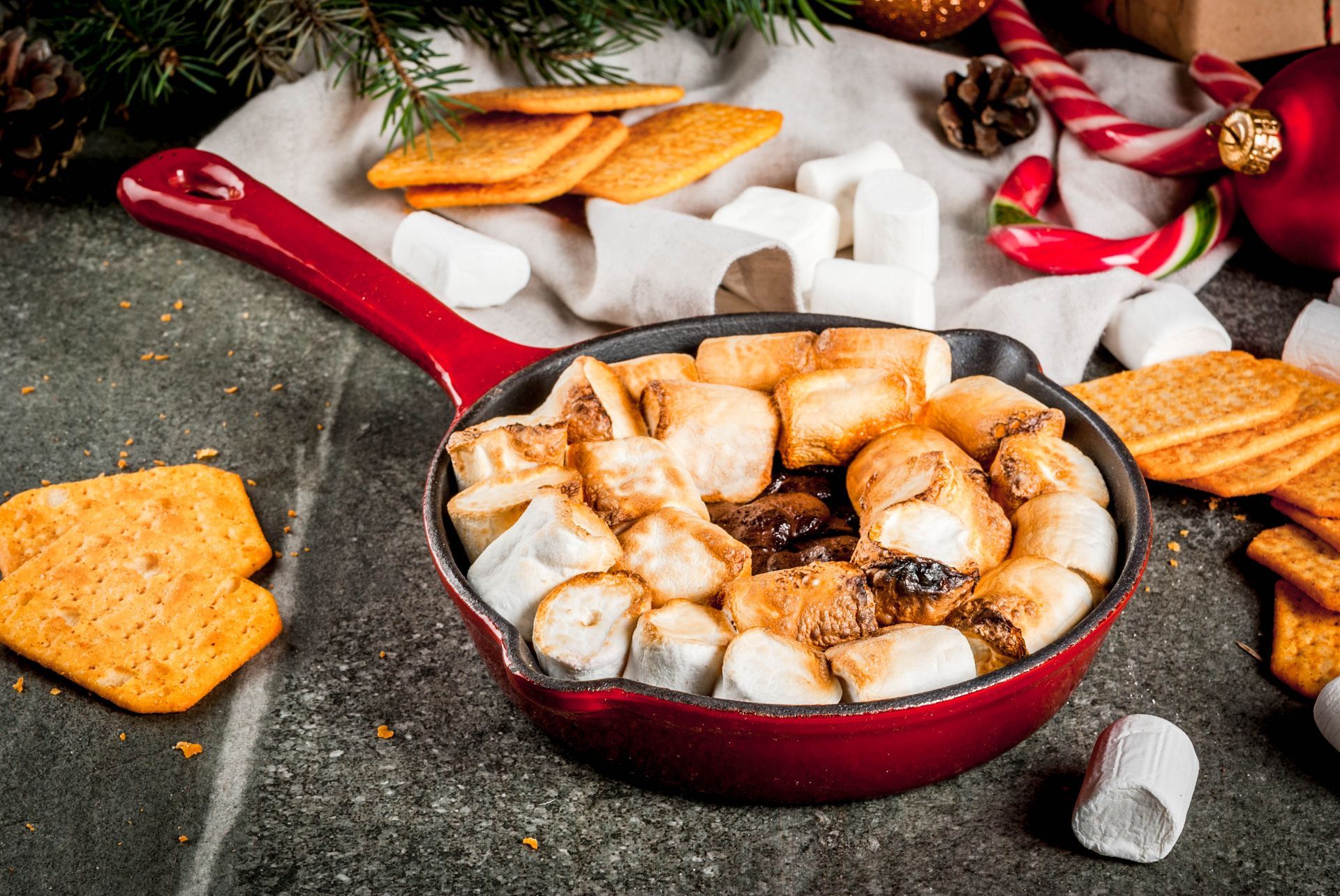 Skillet of toasted marshmallows, with graham crackers, on a festive holiday background.