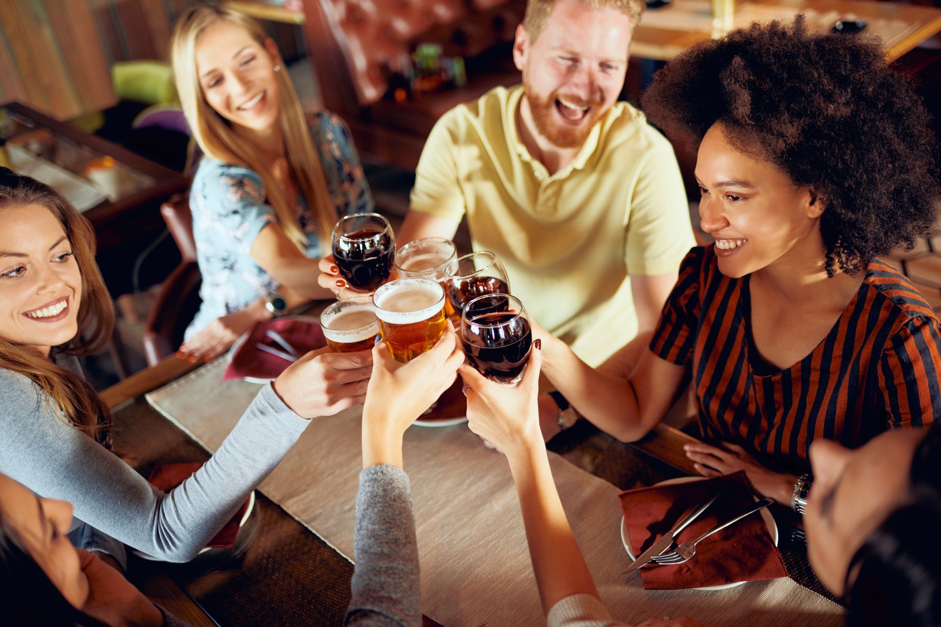 A group of people are sitting around a table toasting with beer and wine.