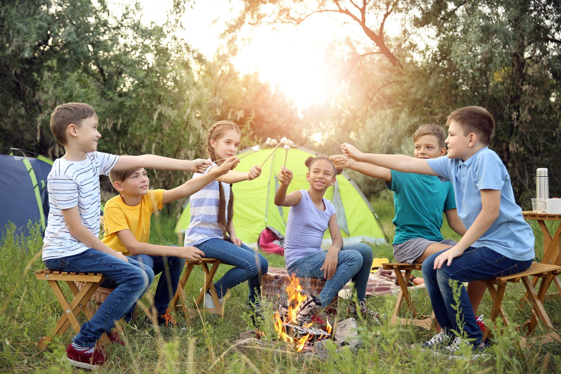 A group of children are sitting around a campfire in front of a tent.