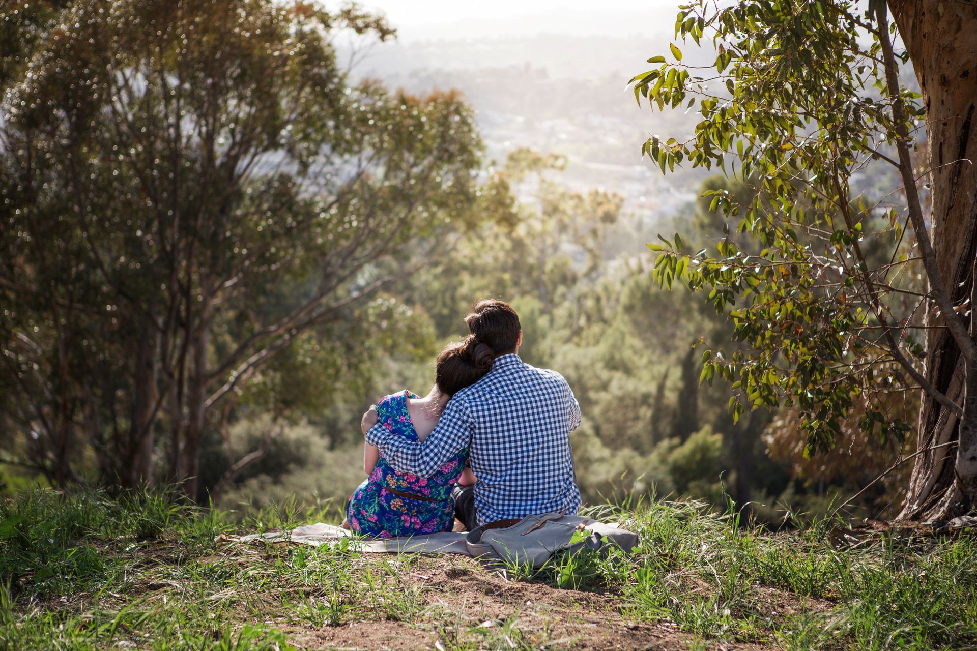 A man and a woman are sitting on a blanket in the woods.