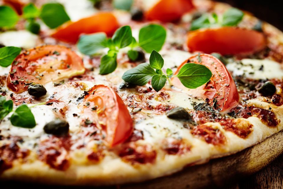 A pizza with tomatoes , cheese , olives and basil on a wooden table.