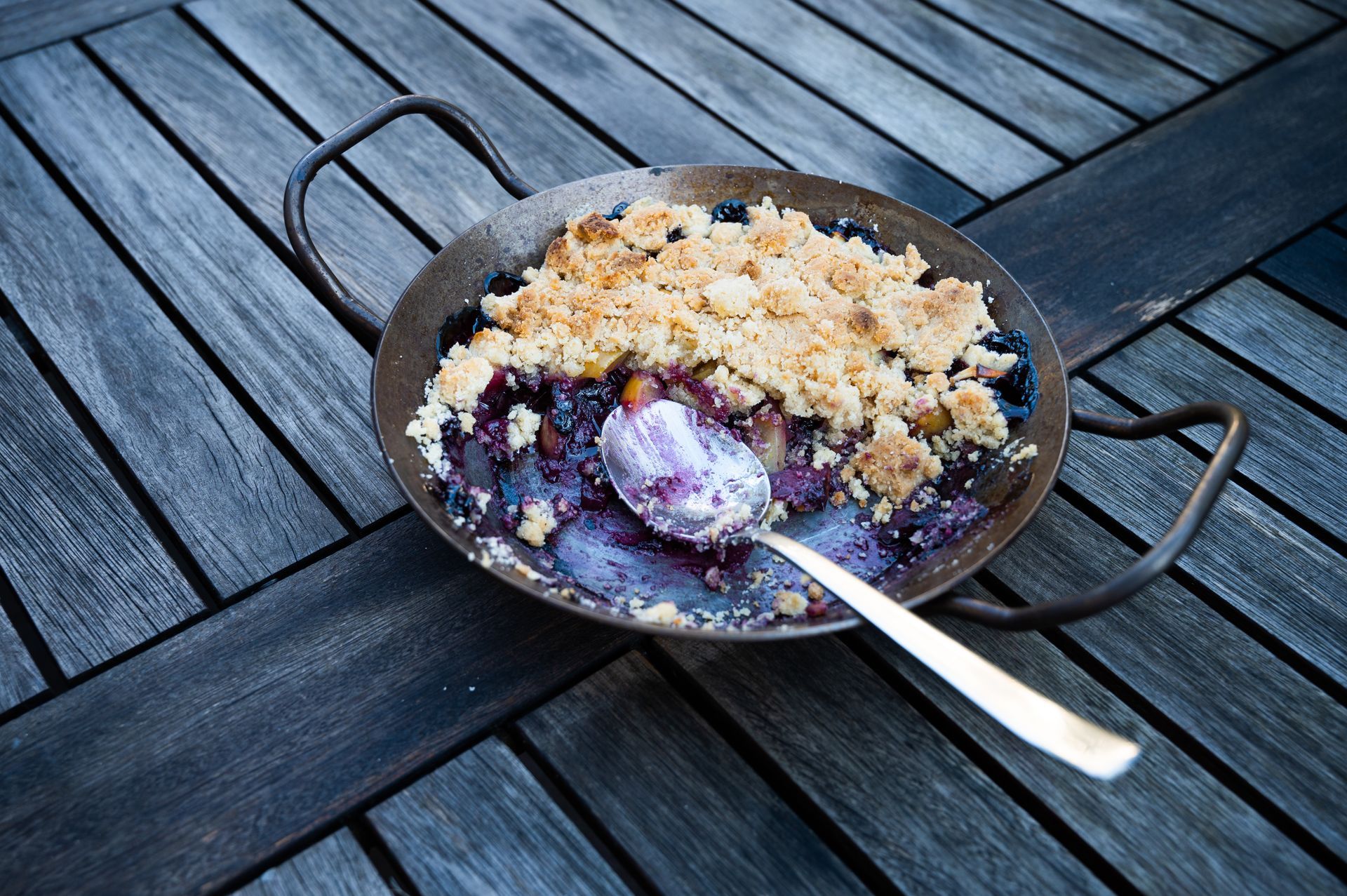 Blueberry crumble in a rustic pan on a wooden table, with a spoonful taken out.