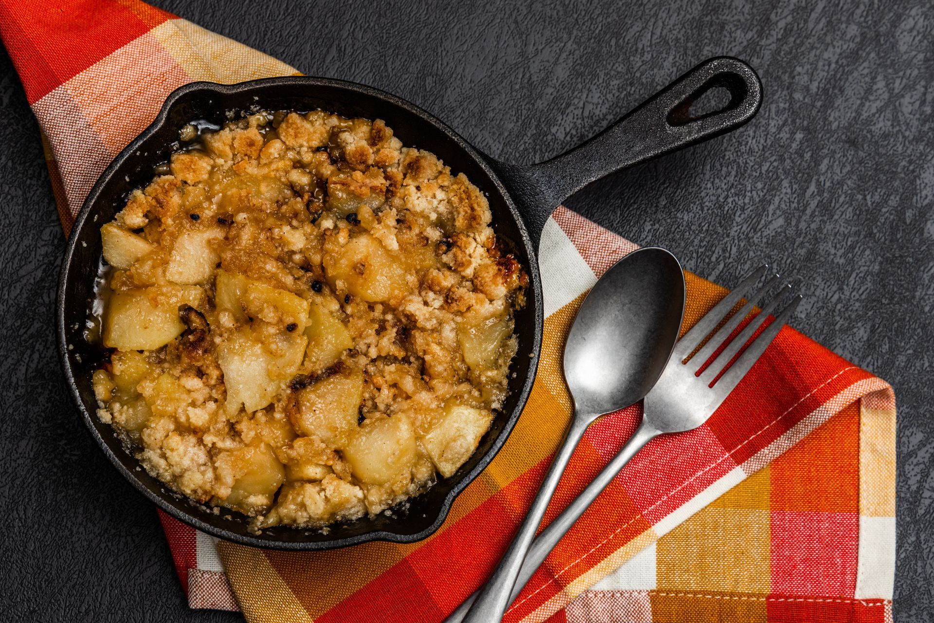 Apple crumble in a cast iron skillet, served with a spoon and fork on a colorful napkin.