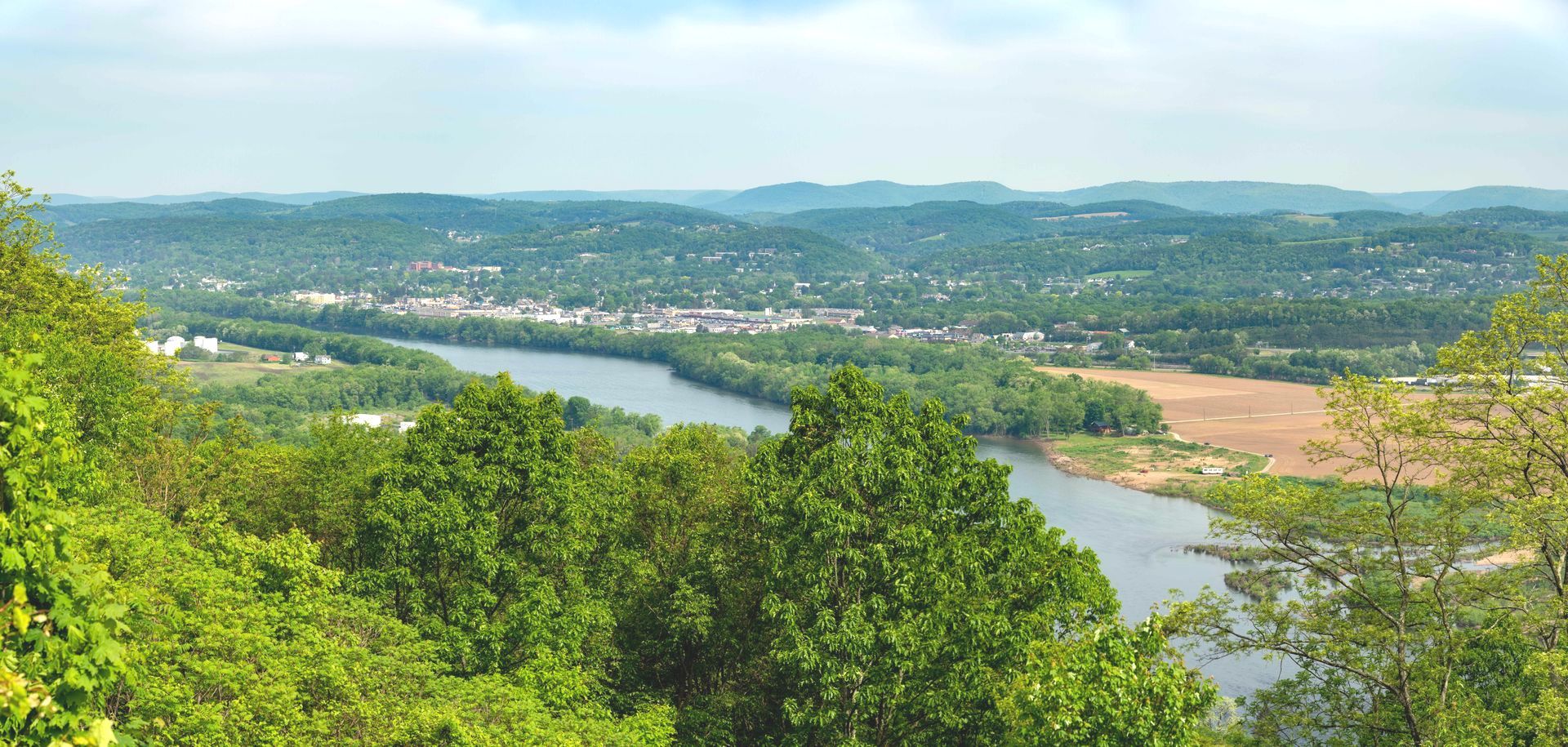 A river surrounded by trees and mountains with a city in the distance.