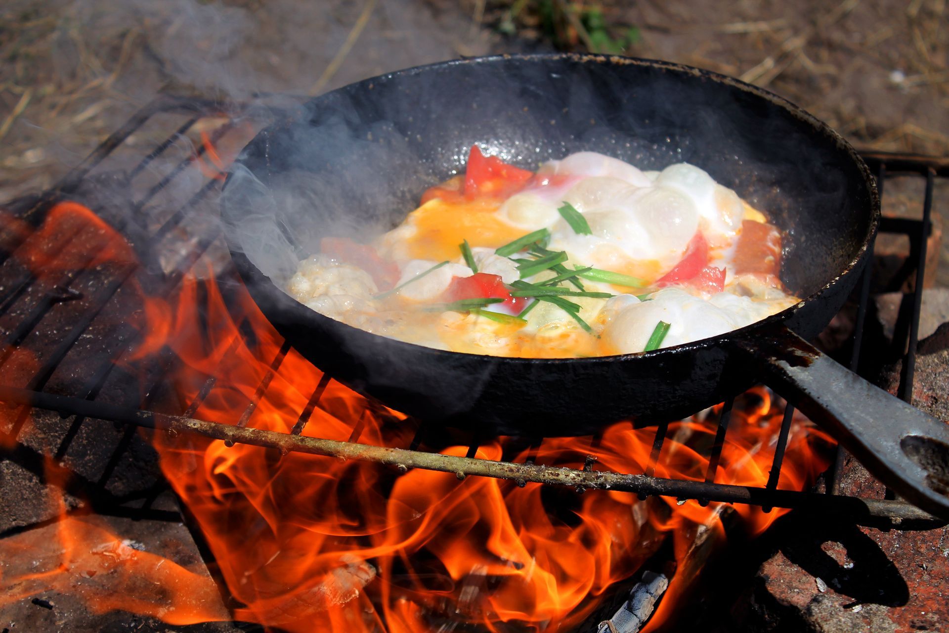 Eggs and vegetables cooking in a pan over a campfire.