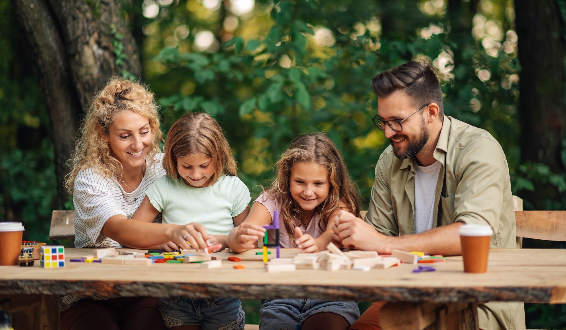 A family is sitting at a table in the woods playing a game.