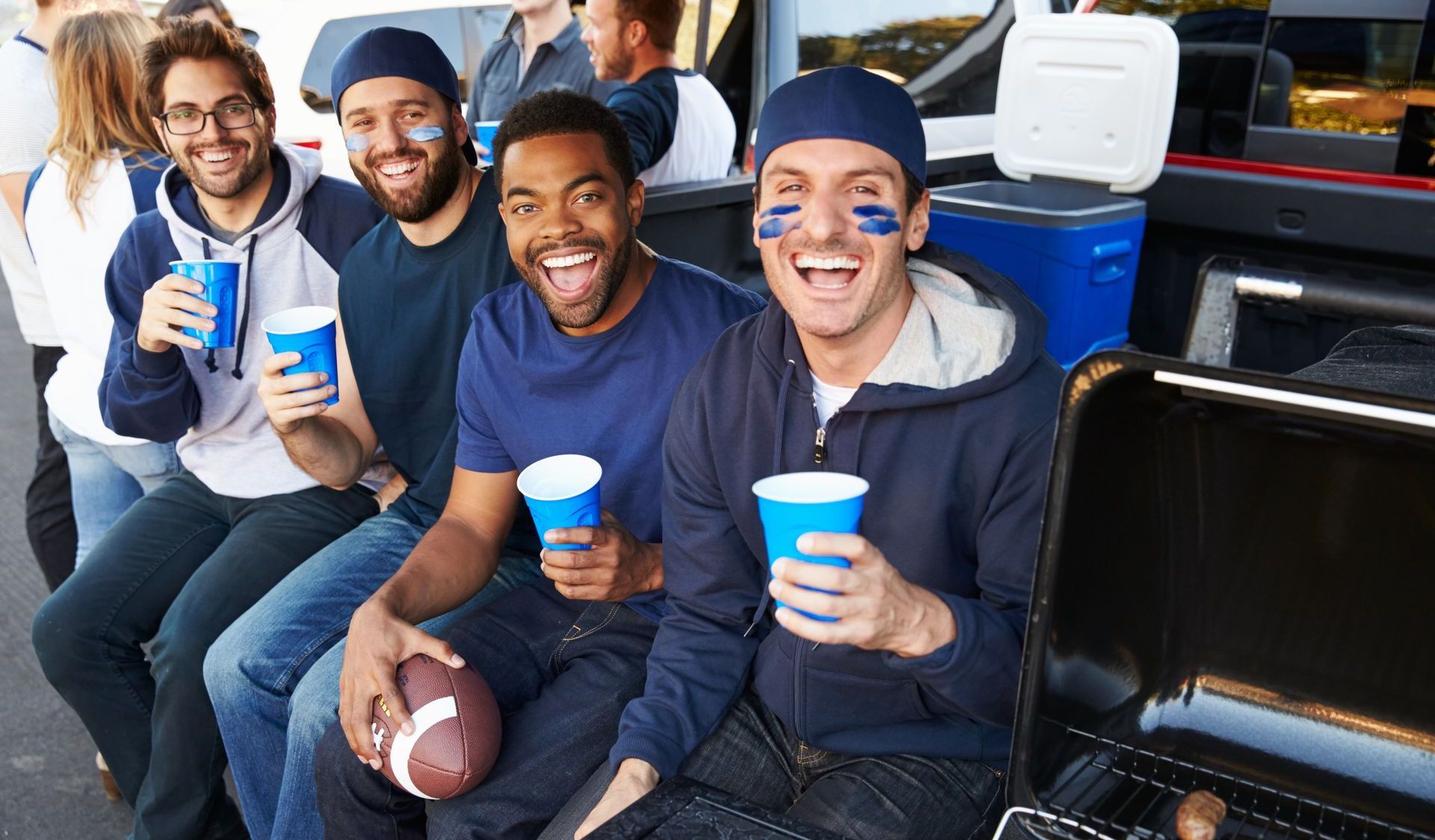 A group of men are sitting in the back of a truck holding cups and a football.