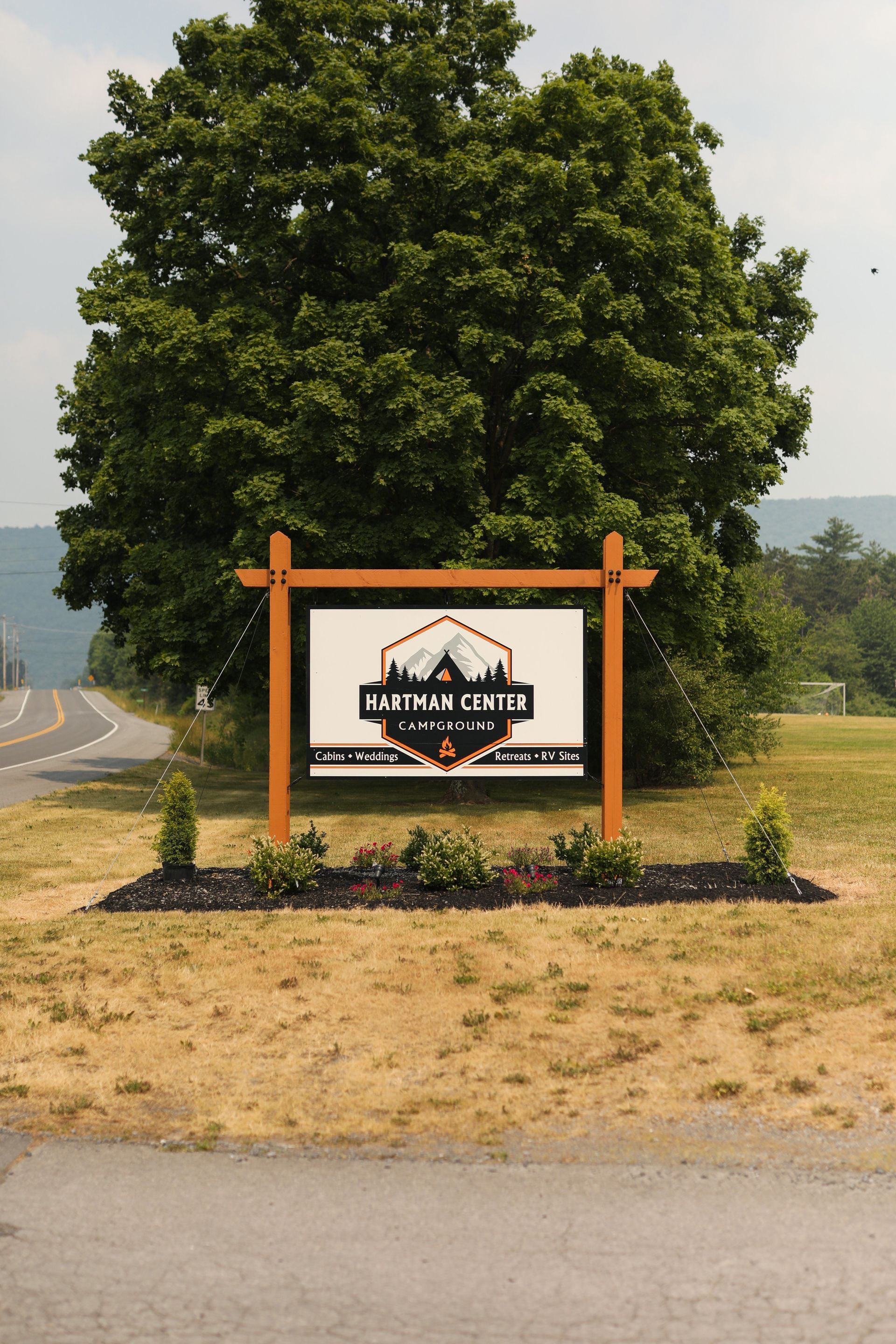 Hartman Center Campground sign sitting in the middle of a field next to a tree.