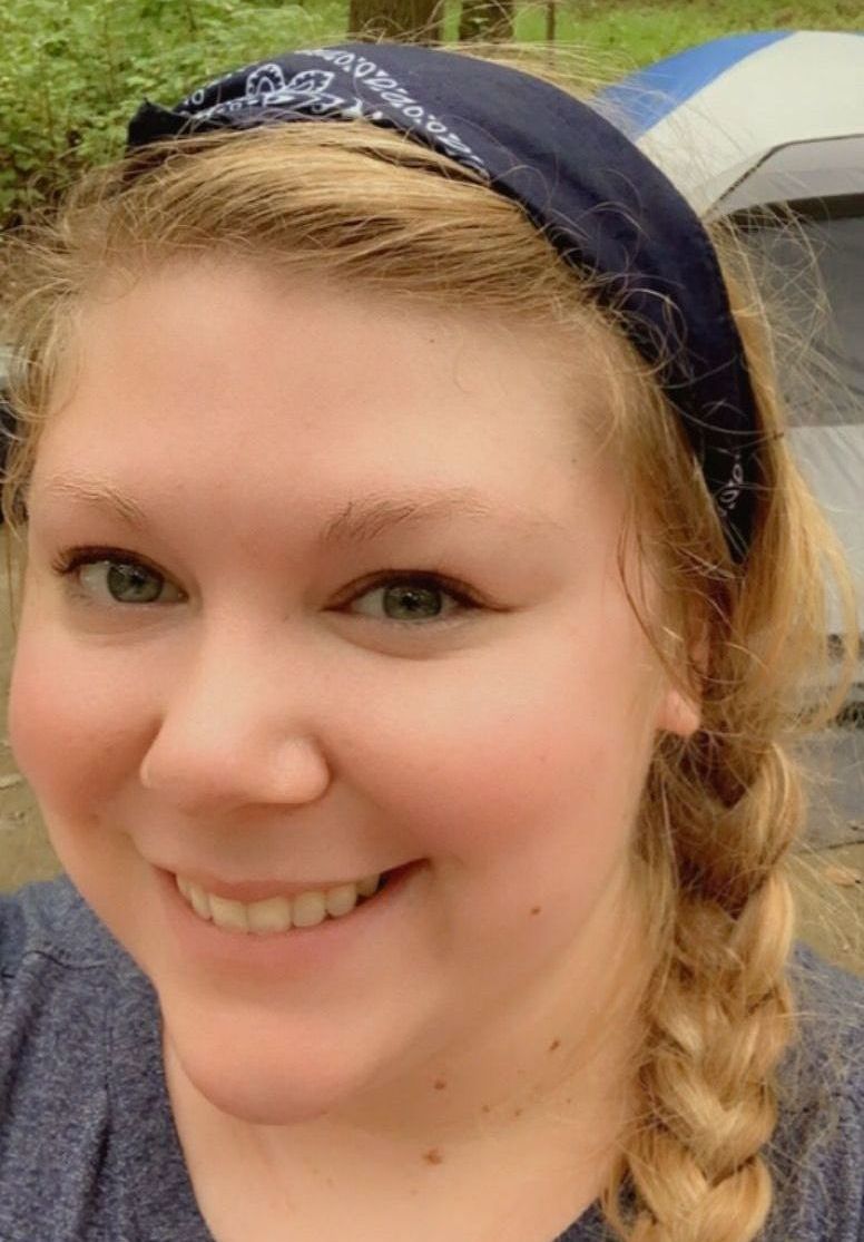 A picture of Amanda wearing a headband is smiling in front of a tent.