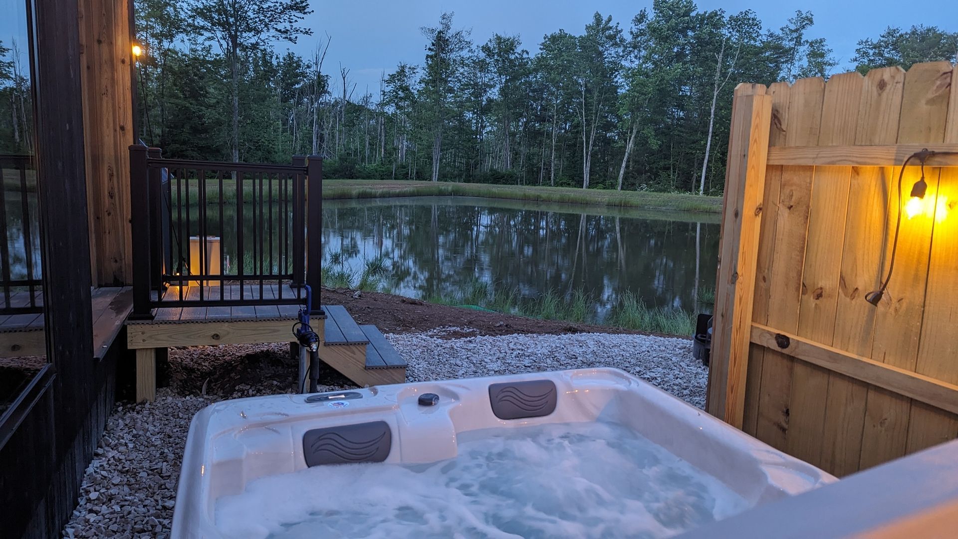 A hot tub is sitting next to a wooden fence next to a lake at a campground.