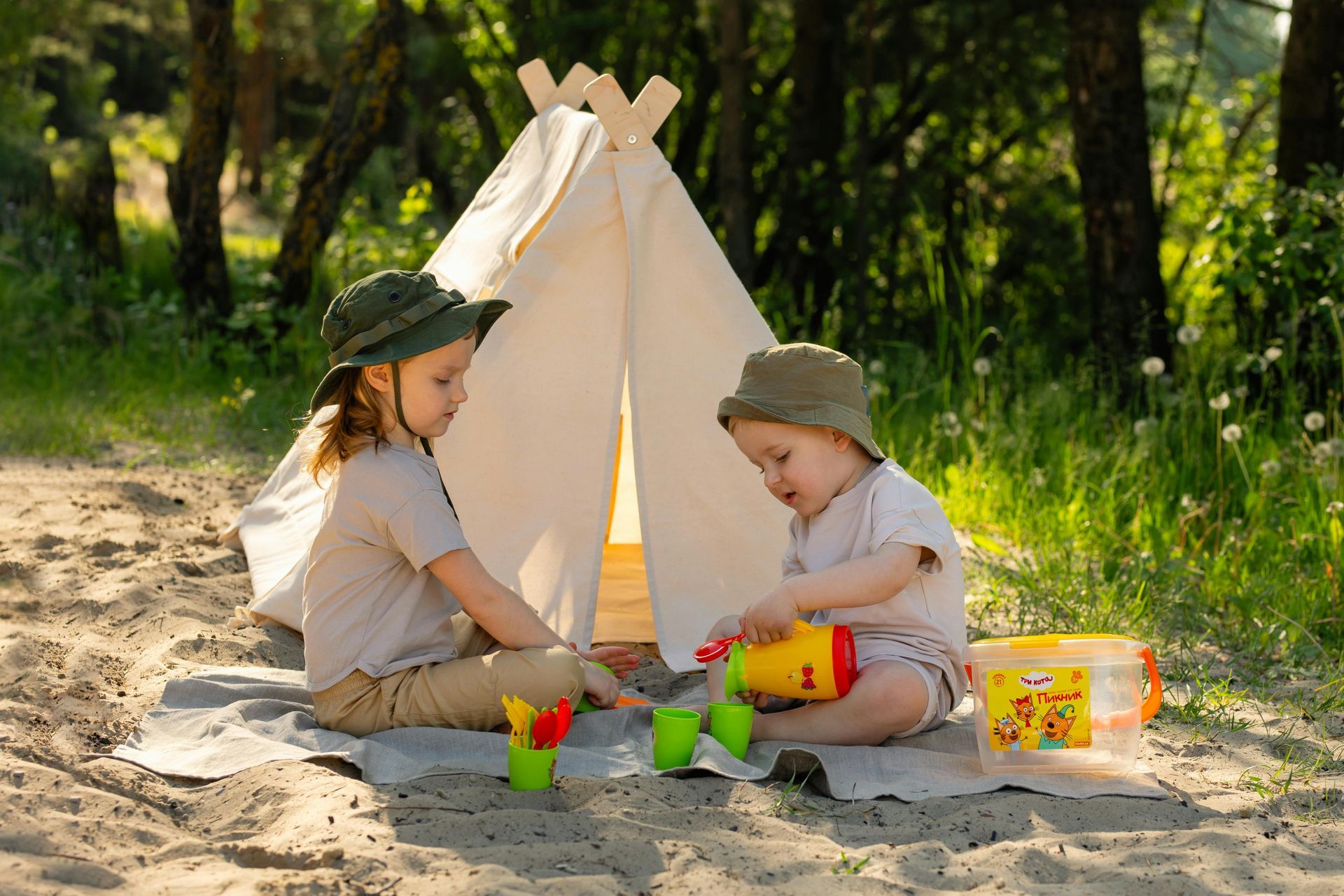 Two little girls are playing in the sand in front of a teepee.